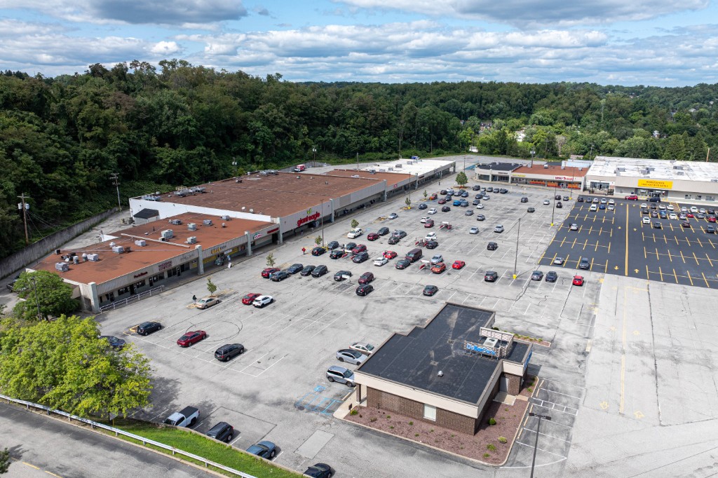 Aerial view of a retail plaza, parking, and surrounding trees
